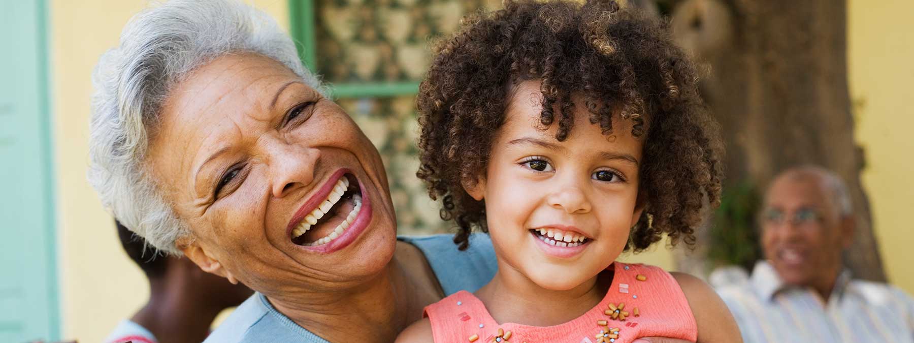 An elderly African American woman laughing while holding her granddaughter