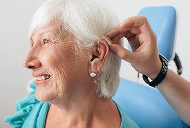 An elderly woman smiles while being expertly fitted with cutting edge hearing aids